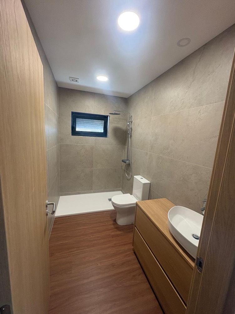 Casa de banho remodelada com revestimento bege de grande formato, base de duche, janela e móvel de lavatório em madeira