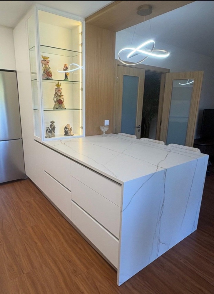 Ilha de cozinha em pedra branca com veios, vitrine iluminada e candeeiro suspenso